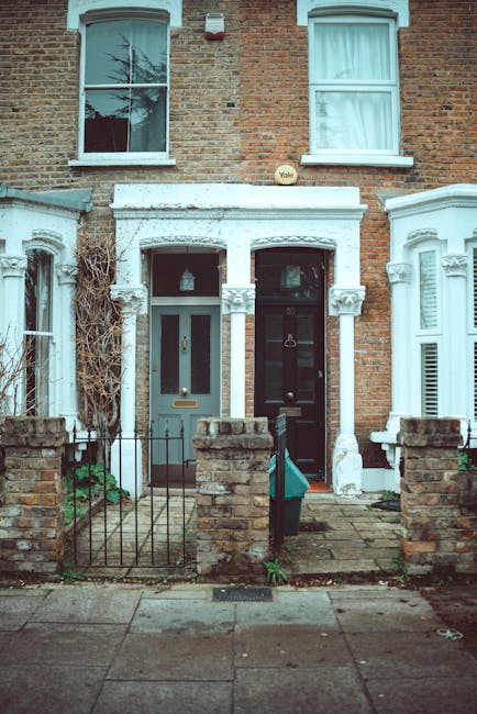 A street scene in Kentish Town with a row of historic multi-storey residential buildings featuring light-colored facades, decorative moldings, and balconies, along with large windows. Several trees li