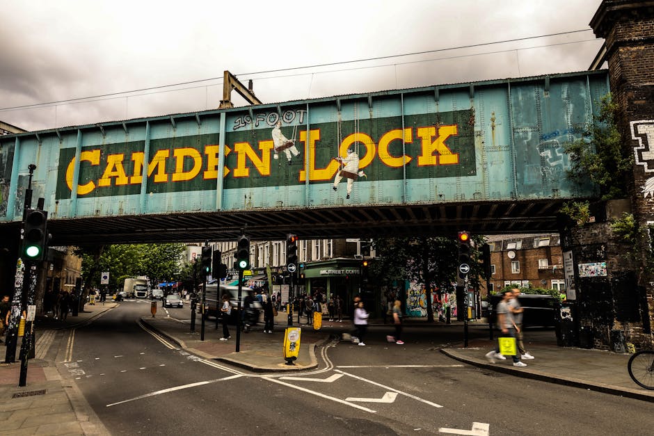 Outside Camden Town Station in London, a busy scene unfolds with a diverse group of pedestrians walking on the pavement and entering the station entrance. The building is constructed of red brick with